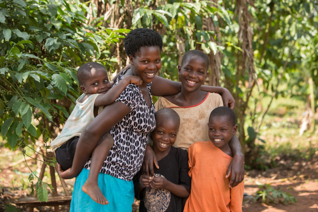 Ruth stands with her children, Alex 5, Jonathan 7, Eva, 11 and George 9, outside their home in Kamuli, Uganda. Ruth was recently reunited with her children through ChildFund's DOVCU scheme for vulnerable children. Photo by Jake Lyell.